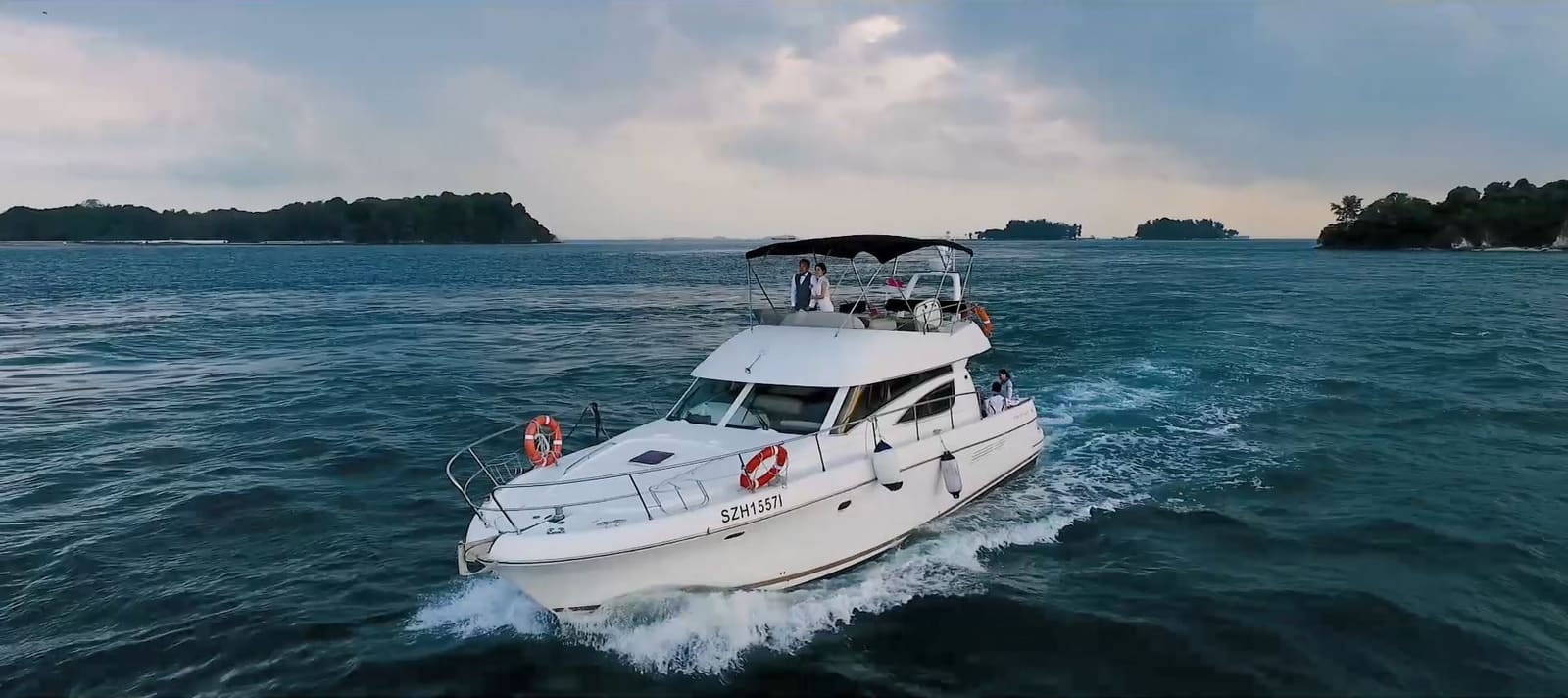 A motor yacht under way off Singapore's Southern Islands in the evening light, a couple standing together on the flybridge
