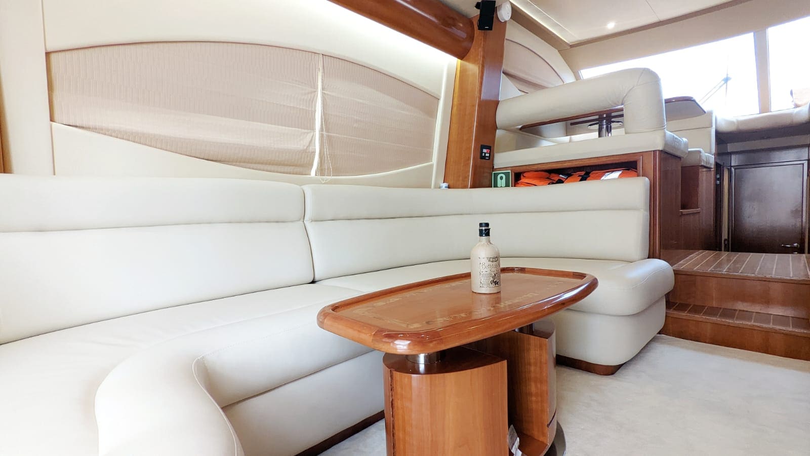 Curved cream leather seating in the saloon, with life jackets stowed in an open locker aft